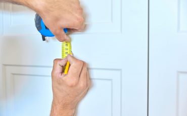 Installation of new cabinet, close-up of hands of working carpenter craftsman with tool, handyman plans place of fastening door handles