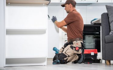 Professional Cabinetmaker in His 40s Finishing Brand New Kitchen Cabinets Installation. Kitchen Remodeling Theme.