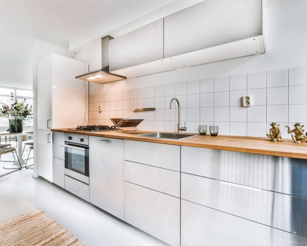 Modern home open plan kitchen with white tiles and cabinets and wooden counter equipped with stove and hood in contemporary apartment